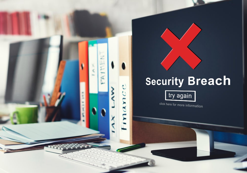 Écran d'ordinateur affichant une alerte de faille de sécurité à côté de classeurs de bureau, soulignant l'importance de la destruction confidentielle d’archives